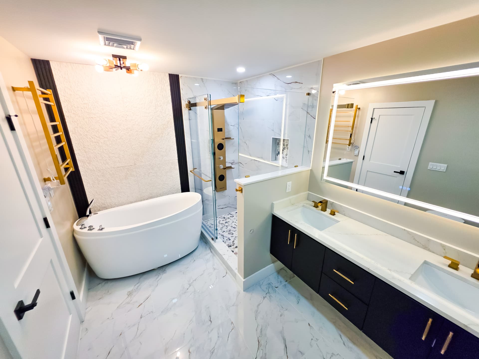 Primary bathroom with freestanding tub, glass shower and backlit mirror over a double vanity