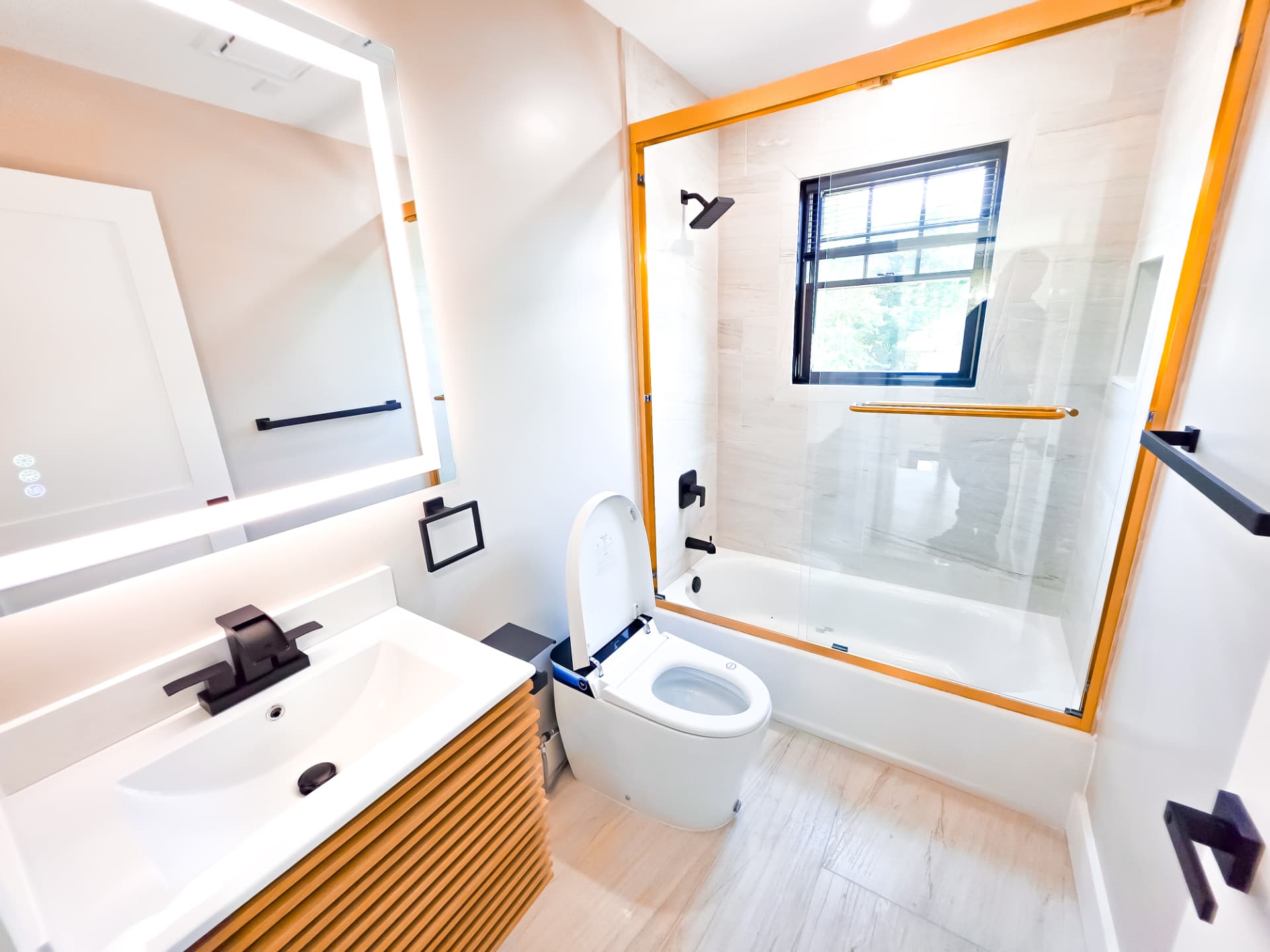 Second full bath with a tub and shower combination, fluted wood vanity, backlit mirror and matte black fixtures