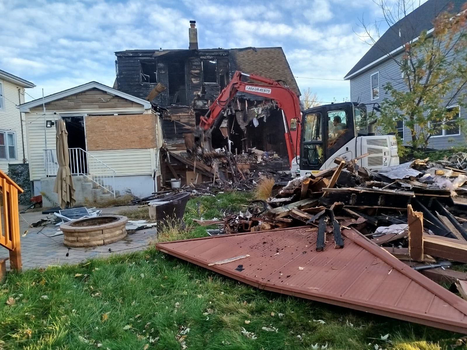 Excavator pulling down the charred rear wall of the fire-damaged house during demolition