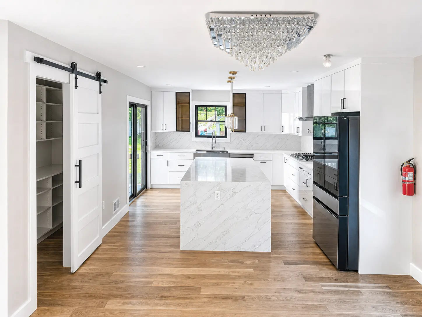 New kitchen with waterfall stone island, white cabinetry and marble-look backsplash