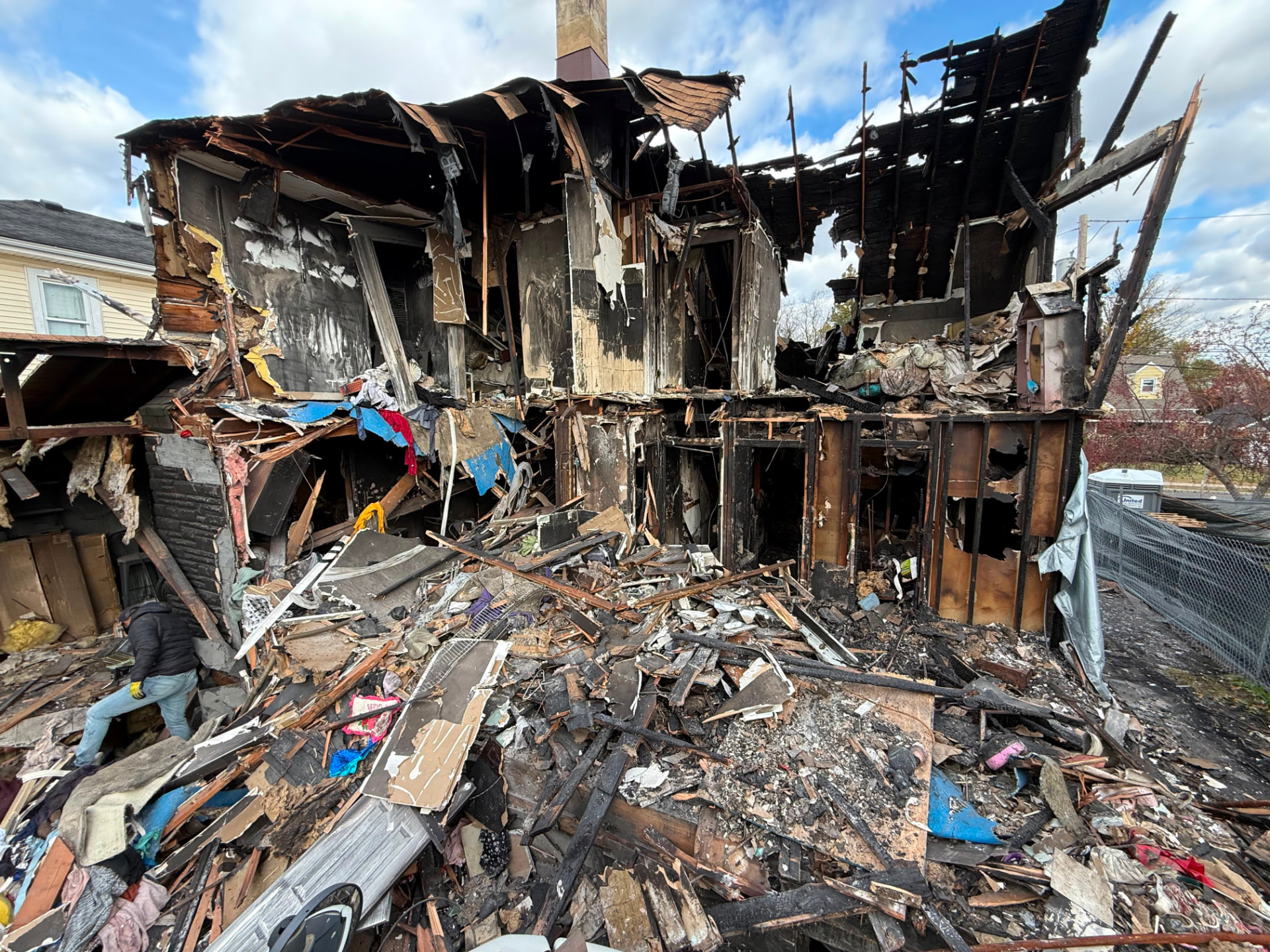 Burned two-story house with the rear wall gone, charred framing exposed and debris piled across the yard